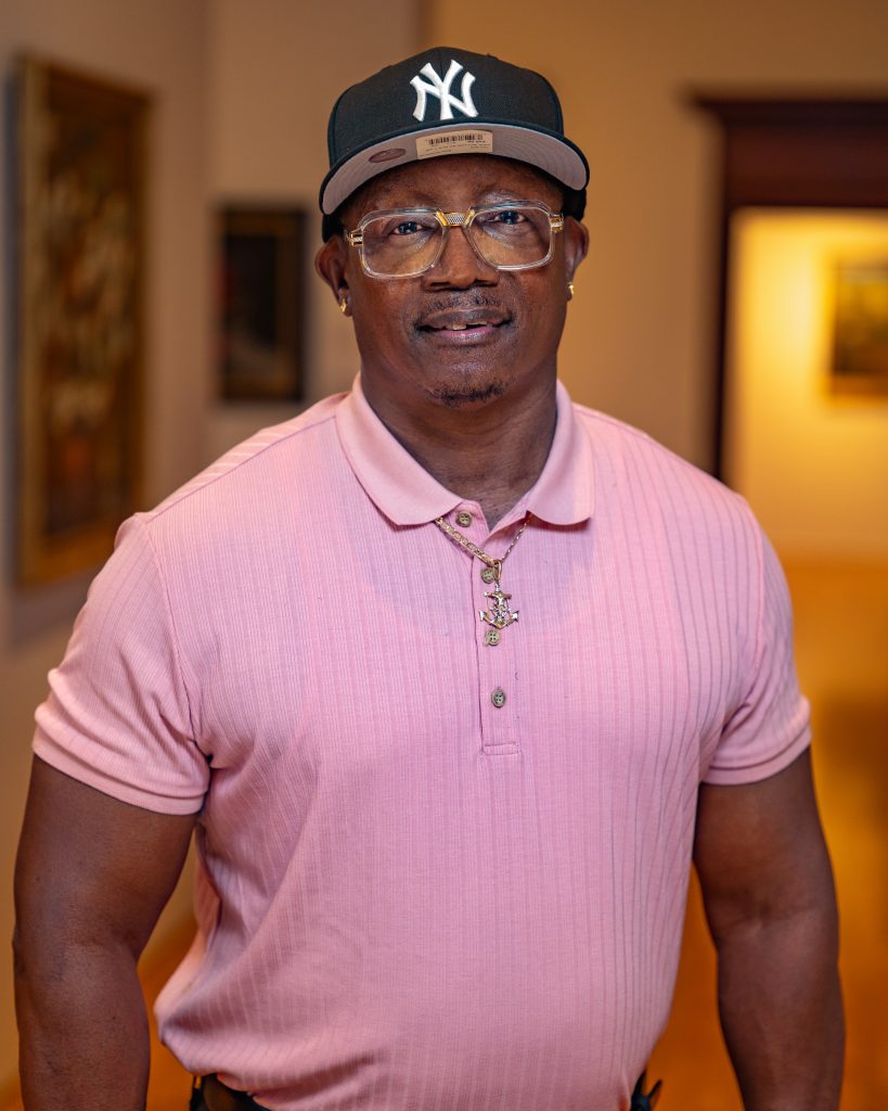 Darryl Dilday in a pink shirt with glasses and a new york yankees cap
