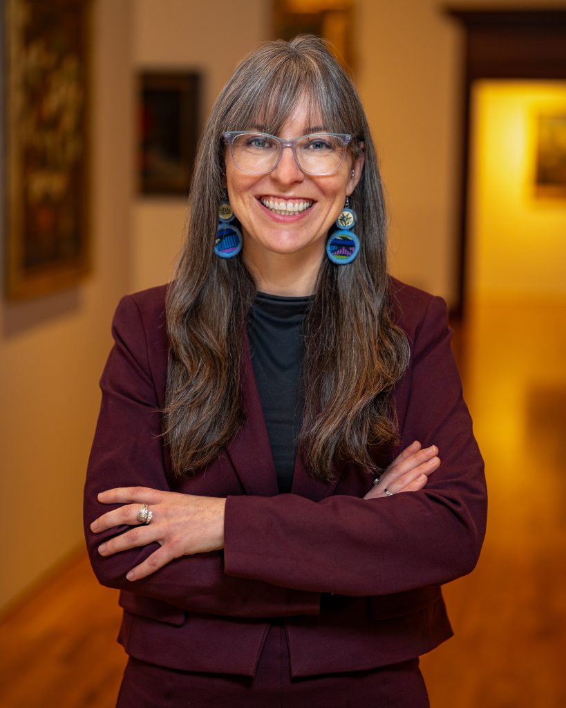 Rebecca McNamara in crimson jacket with blue earrings and glasses